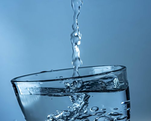 A person pouring clean pure water into a glass in a bright dining room